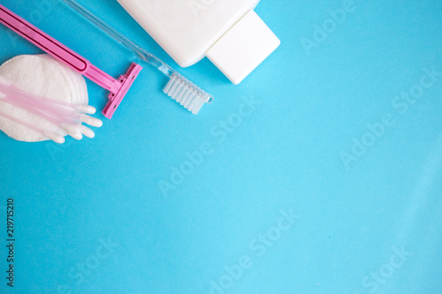 top view personal care products. white bottle, pink razor, ear sticks, cotton pads, toothbrush on blue background. copy space