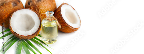 Coconut oil in a bottle with coconuts and green palm tree leaf isolated on a white background. Skincare concept