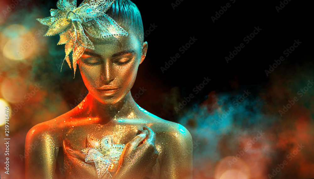 Fototapeta Fashion model woman in colorful bright golden sparkles and neon lights posing with fantasy flower. Portrait of beautiful girl with glowing makeup