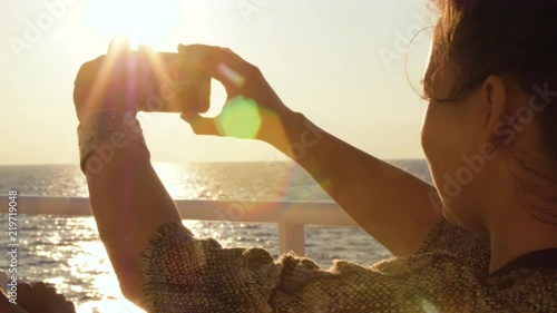 Young woman enjoying sunrise on travel at sea. Taking pictures of the ocean on a ferry on cruise ship vacation