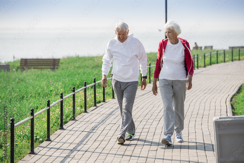 Full length portrait of active senior couple walking in park and smiling happily while chatting on the way, copy space - obrazy, fototapety, plakaty 