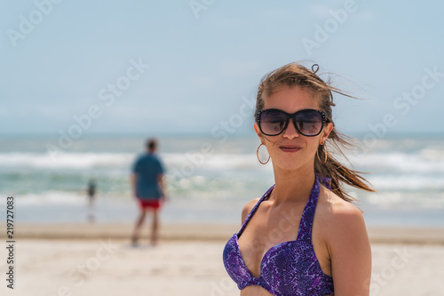 Young Italian American Model in Purple Bikini and Dark Sunglasses and Hair Blowing in Wind Smiling at Camera