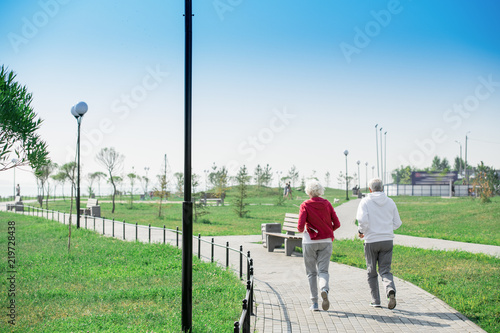 Rear  view portrait of active senior couple running together in park, copy space