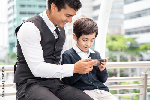 Father teaching boy to use smartphone at city. People with technology concept.