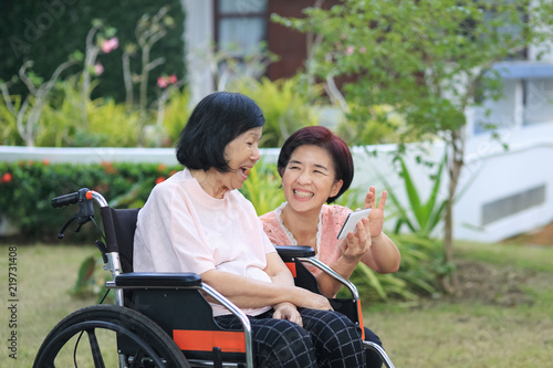 Daughter caring for the elderly asian woman ,do selfie, happy, smiles in backyard.