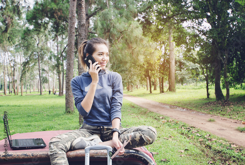 Woman use smart phone in outdoor.Asian girl relaxing on the car roof in her spring road trip, carefree and enjoying freedom and travel. travel concept scene.