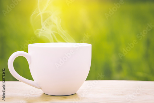 hot coffee cup on wooden table over nature green rice field background with morning sunlight 