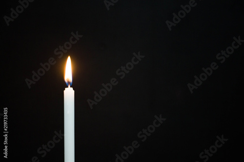One light candle burning brightly on black background