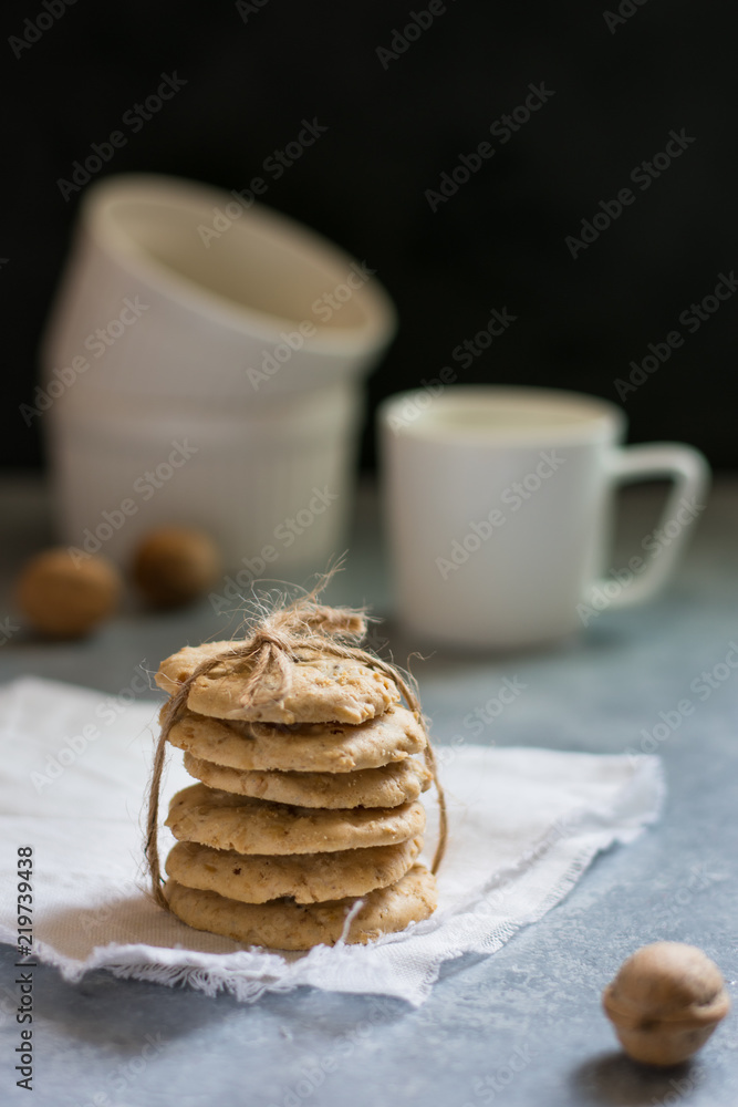 Oatmeal cookies tied with a rope on a white linen napkin, white cup and walnuts in the background