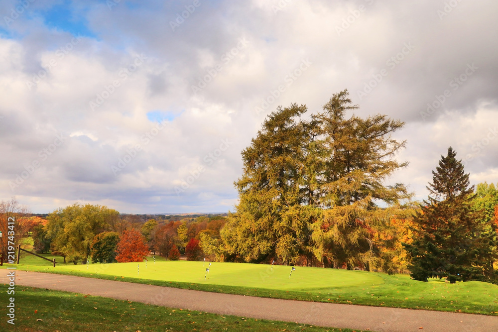 Beautiful Midwest autumn nature background. Scenic view with cloudy sky over golf course. Flags on a green lawn and colorful trees in sunlight. Leisure activity and lifestyle background. Beautiful Midwest autumn nature background. Scenic view with cloudy sky over golf course. Flags on a green lawn and colorful trees in sunlight. Leisure activity and lifestyle background.