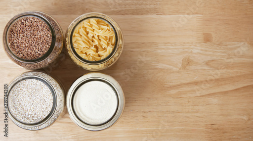 Various uncooked cereals, grains, and pasta for healthy cooking in glass jars on wooden table. Top view. Clean eating, balanced dieting food. Copy space.