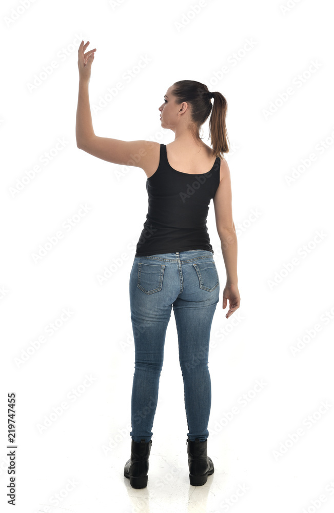 full length portrait of brunette girl wearing black single and jeans. standing pose with back to the camera. isolated on white studio background. full length portrait of brunette girl wearing black single and jeans. standing pose with back to the camera. isolated on white studio background.