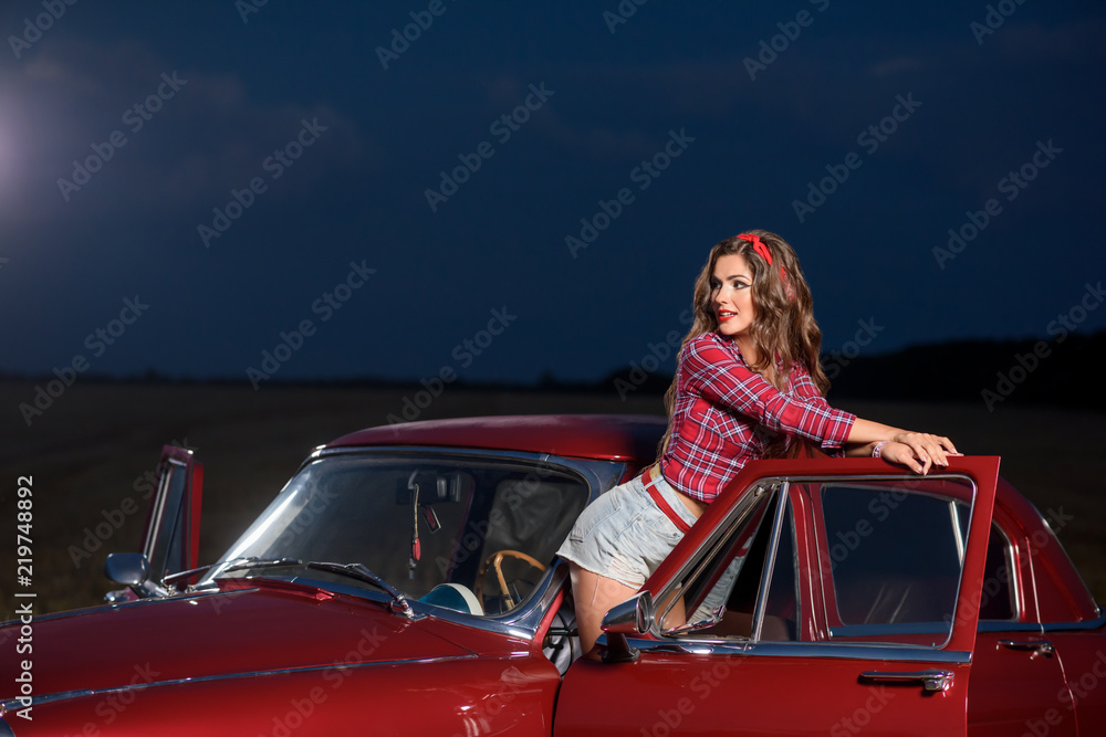 Sexy pin up girl posing near red retro, old fashioned car in the night's  field. Stock Photo | Adobe Stock
