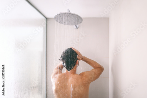 Fototapeta Man taking a shower washing hair with shampoo product under water falling from luxury rain shower head
