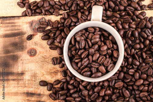 Cup of coffee full of coffee beans on wood background, top view