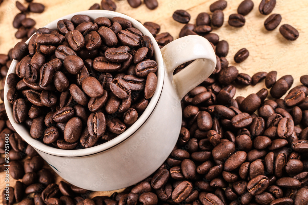 Fototapeta premium Cup of coffee full of coffee beans on wood background, side view