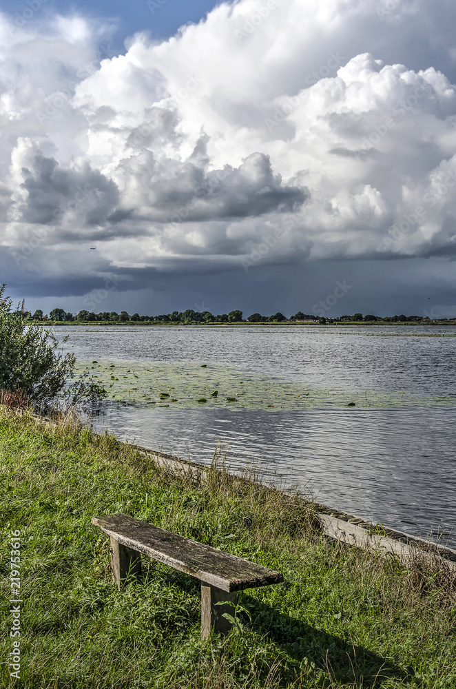 Somewhat cranky wooden bench by a lake with a view towards a spectacular cumulus cloudscape near Ankeveen, The Netherlands Somewhat cranky wooden bench by a lake with a view towards a spectacular cumulus cloudscape near Ankeveen, The Netherlands