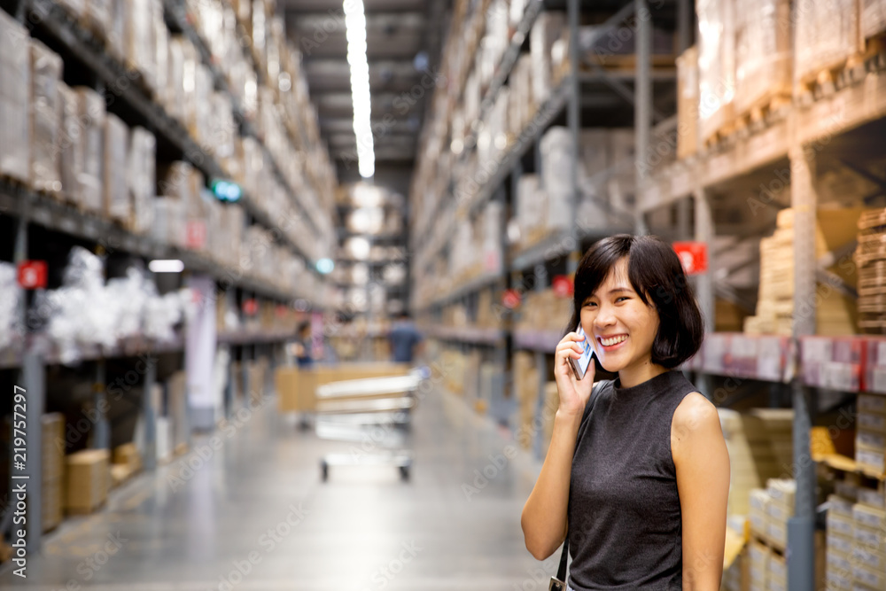 Fototapeta premium An asian woman doing shopping online via mobile phone in the warehouse with blurred bokeh lights background.