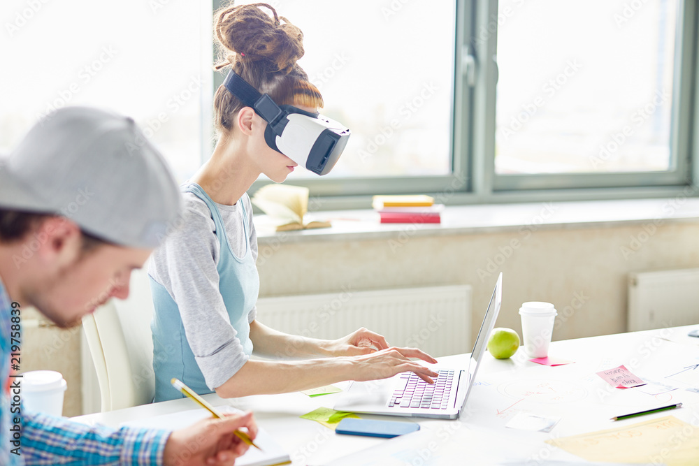 Serious concentrated startupper in VR simulator typing laptop while testing new app, students working on project Serious concentrated startupper in VR simulator typing laptop while testing new app, students working on project