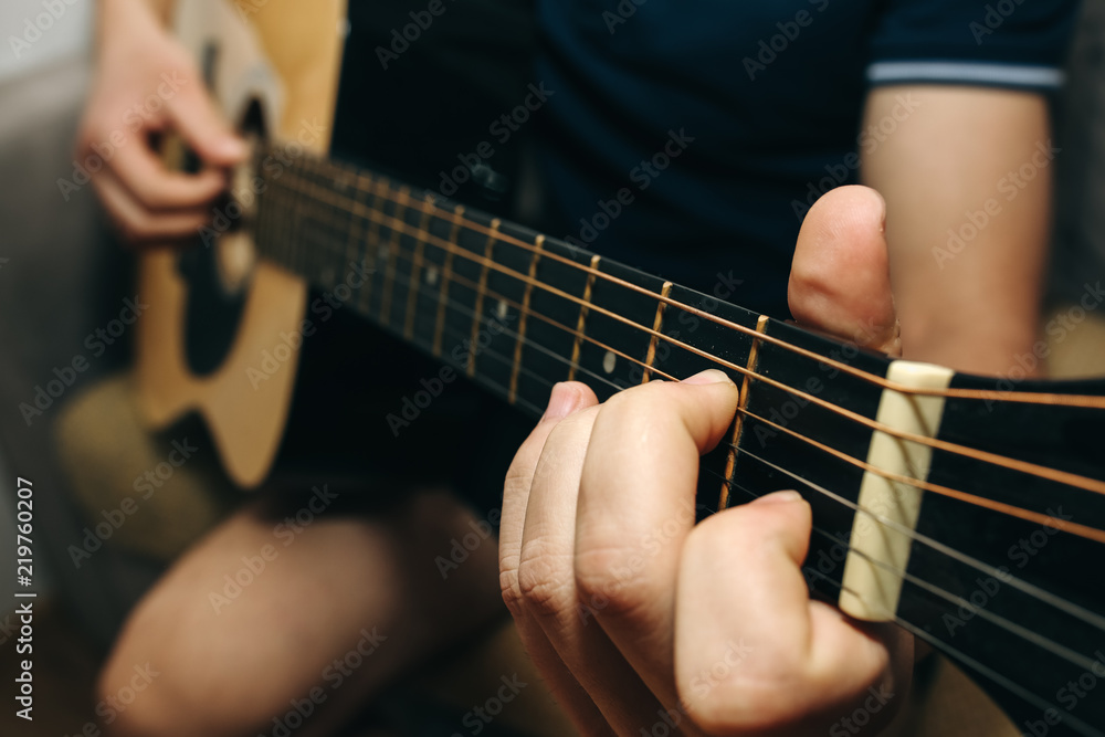 Man at home is playing the guitar. Guys hands are taking the chord on strings. Music making lifestyle concept. Free time hobby for everyone. Retro guitar photo.
