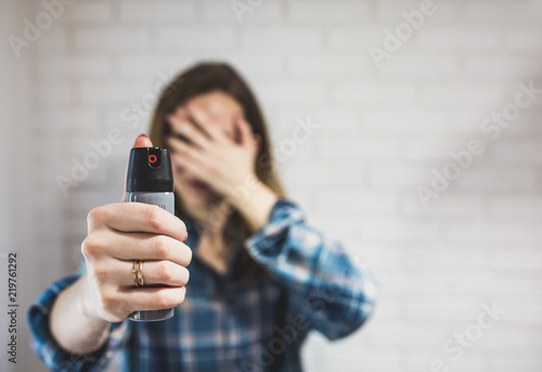 Married woman is holding pepper spray canister for personal protection. Girl covers her face with hands. White background behind. Self-defense photo. Copy space place.