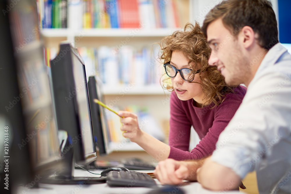 © pressmaster - Female college student showing computer program to her classmate during a lesson at computer class at college