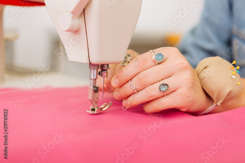 Sewing machine. Professional female dressmaker holding a thread and fixing it near the sewing foot of her sewing machine