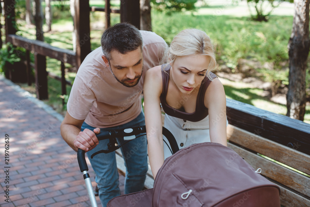 parents looking at baby carriage in park parents looking at baby carriage in park