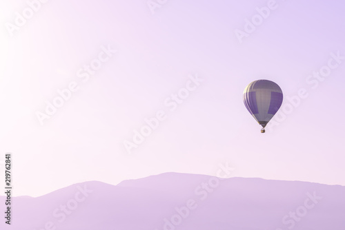 Hot air balloon in the pink sky above soft sunrise mountains silhouettes with copy space