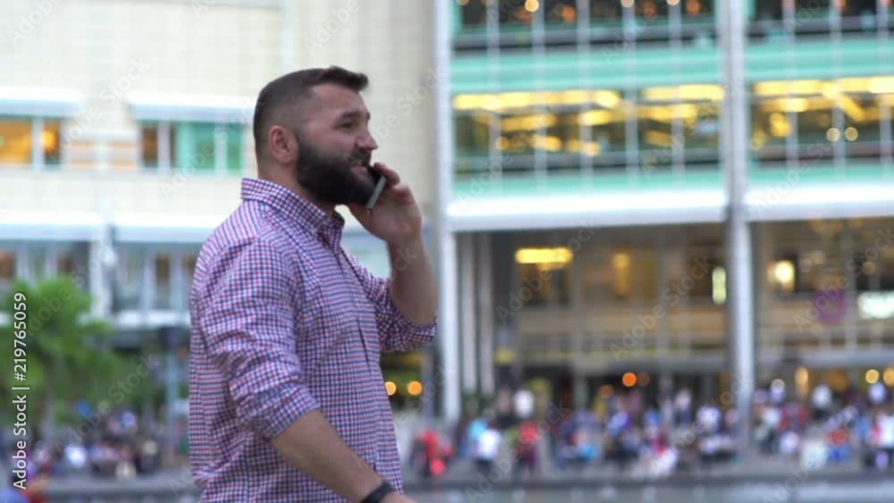 Young man talking on cellphone while walking by fountain in city
