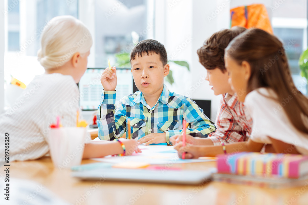 Excited. Smart confident schoolboy telling a story while being with classmates