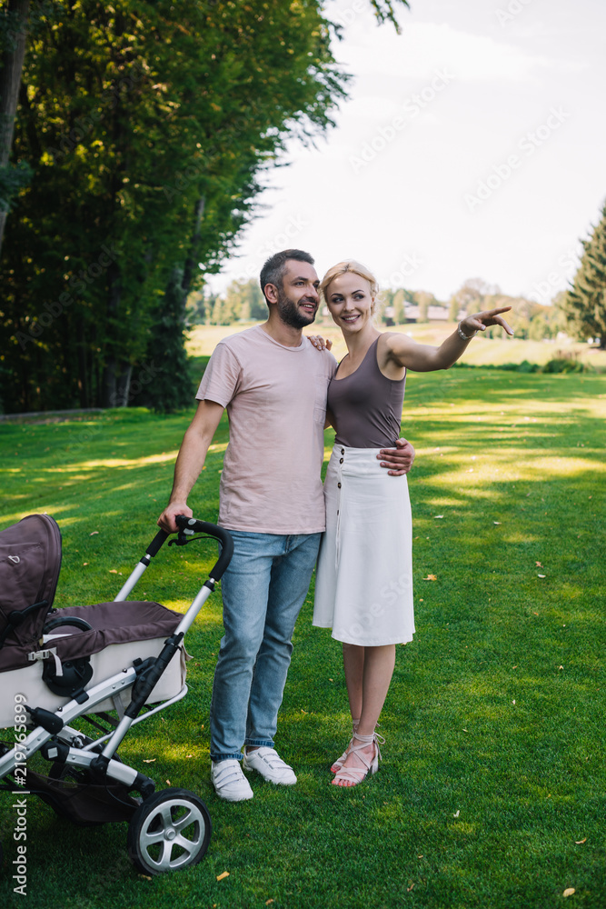 Fototapeta premium wife pointing on something to husband near baby carriage in park