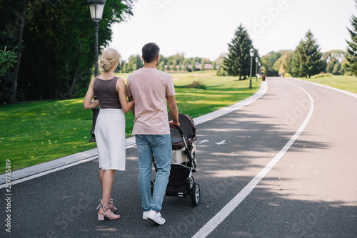 back view of parents walking with baby carriage on road in park