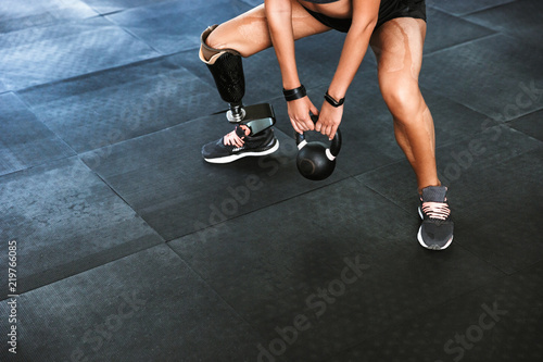 Portrait of sporty disabled woman with prosthesis in tracksuit doing crossfit exercises, and lifting dumbbell in gym © Drobot Dean