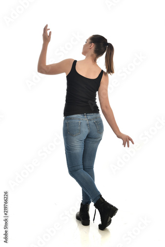 full length portrait of brunette girl wearing black single and jeans. standing pose with back to the camera. isolated on white studio background.