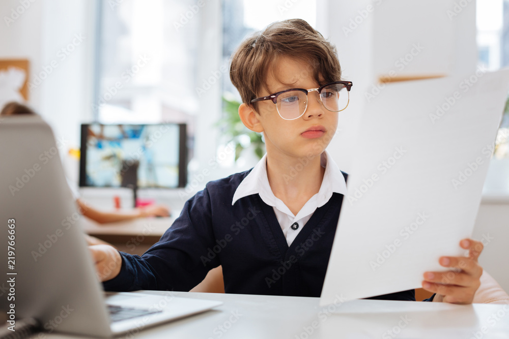 Documents. Clever attentive schoolboy working on a document while sitting in a room Documents. Clever attentive schoolboy working on a document while sitting in a room