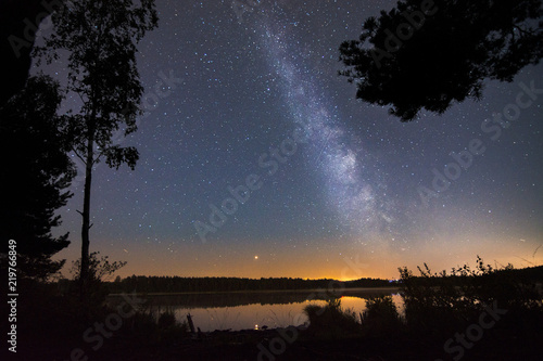 Glowing milky way over a still lake with sunset in the background. Tropical summer nights with million stars above and colorful sky. 