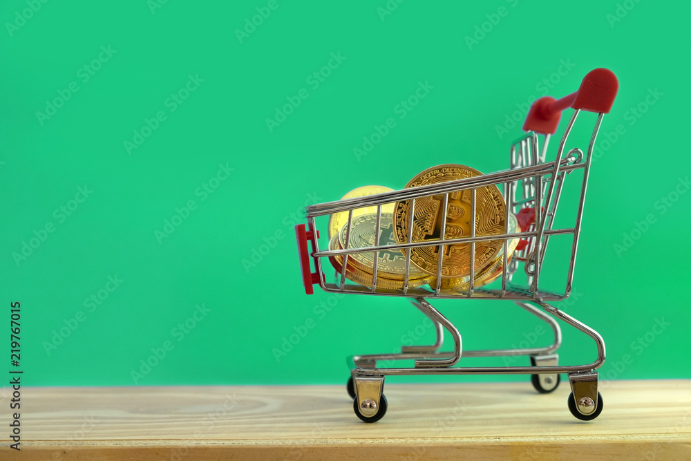 Bitcoins in basket of model shopping cart on green background for virtual money, blockchain technology and cryptocurrency concept.