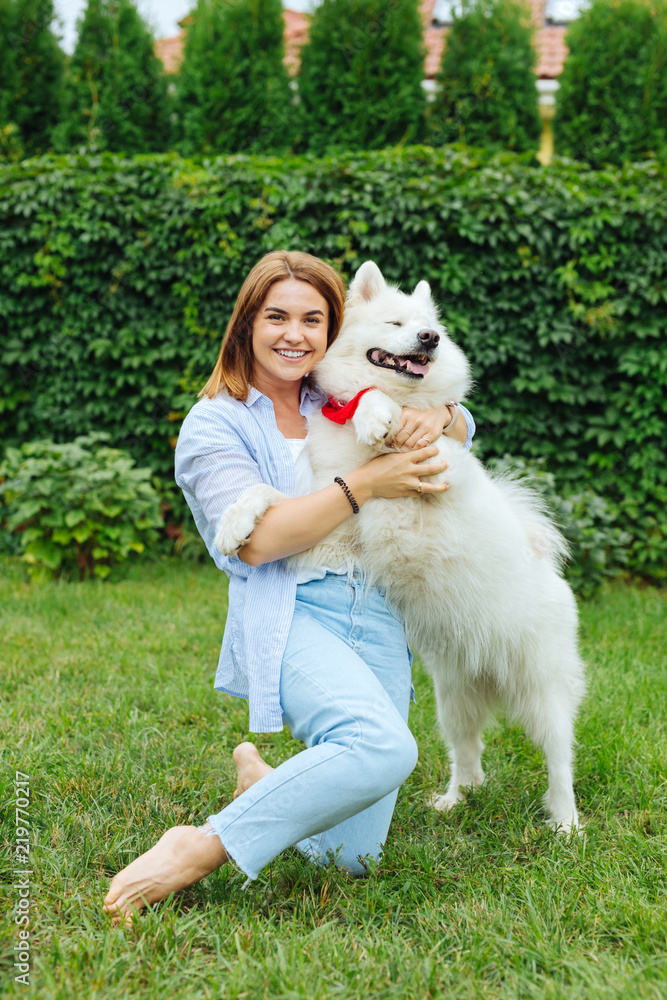 Meeting dog. Cheerful woman wearing stylish jeans and striped shirt smiling while meeting her white dog Meeting dog. Cheerful woman wearing stylish jeans and striped shirt smiling while meeting her white dog