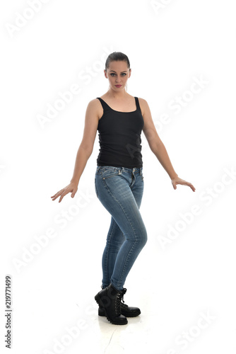 full length portrait of brunette girl wearing black single and jeans. standing pose facing the camera. isolated on white studio background.