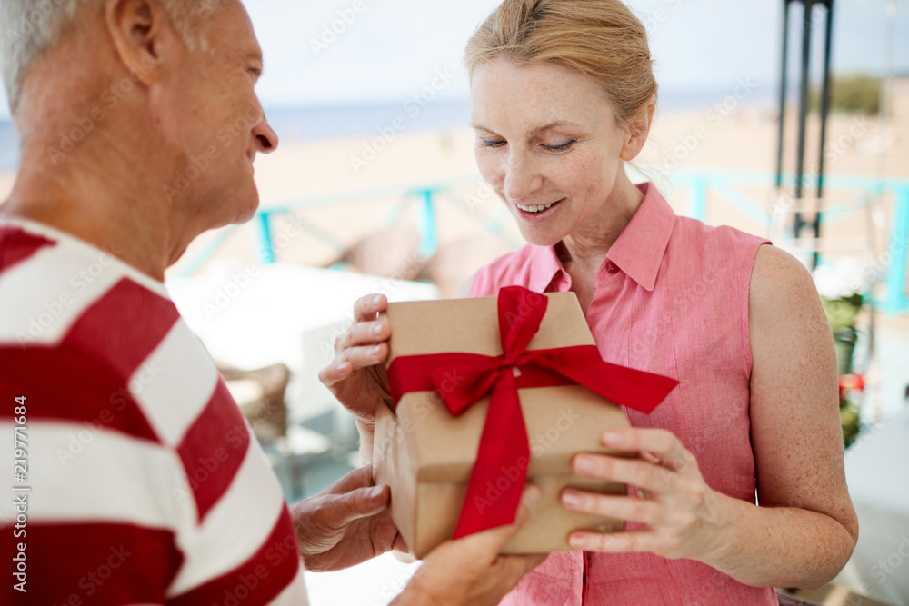 Happy aged woman taking look in giftbox given by her husband for her birthday or anniversary Happy aged woman taking look in giftbox given by her husband for her birthday or anniversary