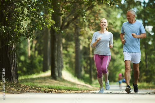 Active and healthy aged couple running in natural environment on summer morning
