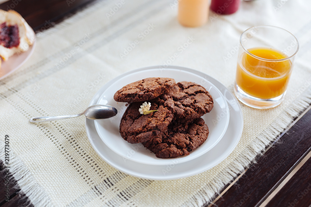Chocolate cookies. Four chocolate cookies lying on little white plate near glass of freshly squeezed orange juice Chocolate cookies. Four chocolate cookies lying on little white plate near glass of freshly squeezed orange juice