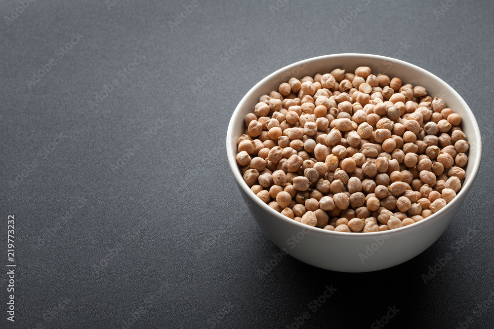 dry chickpeas in white bowl isolated on dark background