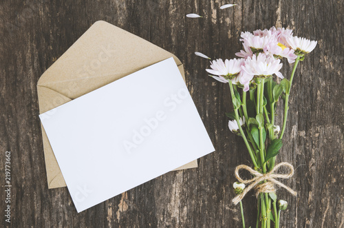 Blank greeting card with brown envelope and Mum flowers on wooden table photo