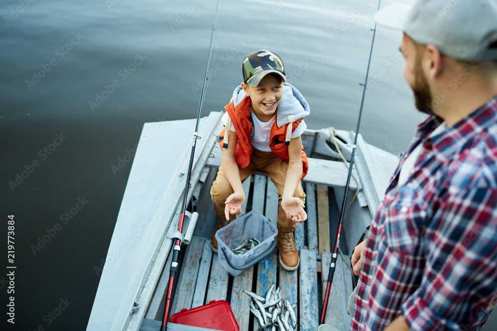 Happy son showing catch to his father while they are in the boat Happy son showing catch to his father while they are in the boat