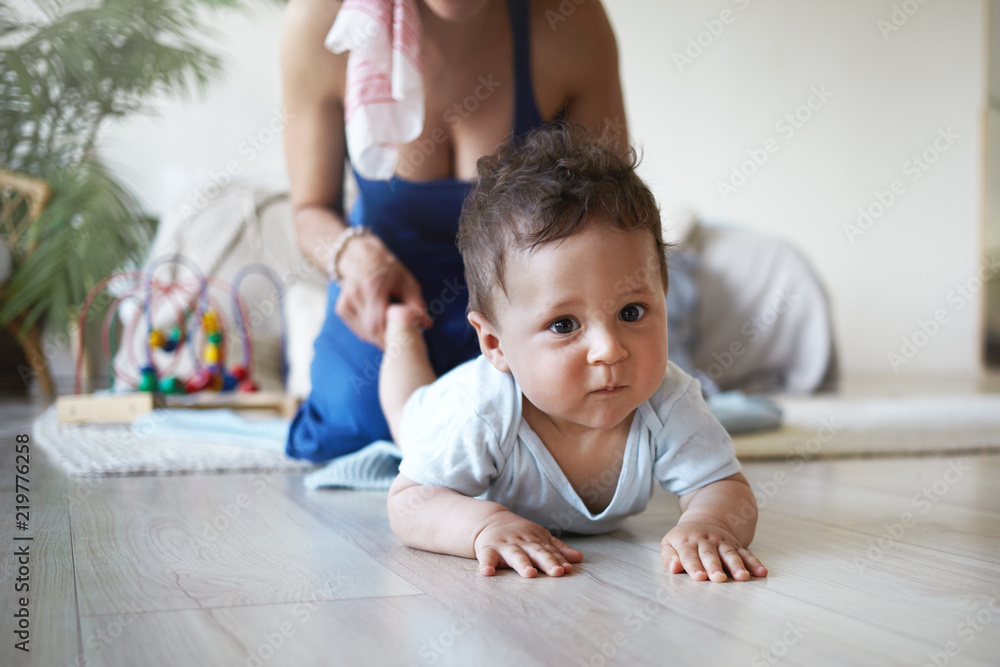 Cropped shot of positive young mixed race female with charming smile holding toes of her baby son while playing with him on floor at home. Parenting, childhood, maternity and family bonding concept Cropped shot of positive young mixed race female with charming smile holding toes of her baby son while playing with him on floor at home. Parenting, childhood, maternity and family bonding concept