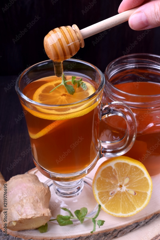 Tea with lemon and mint in a glass. Honey is dripping from the wooden spoon Tea with lemon and mint in a glass. Honey is dripping from the wooden spoon