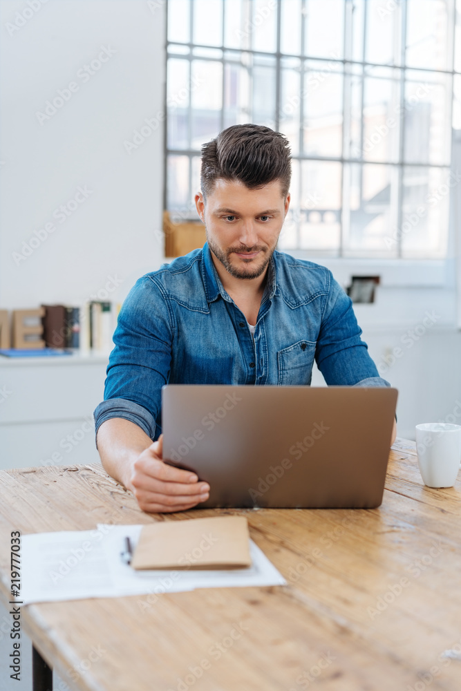 mann sitzt am schreibtisch im büro und schaut auf sein notebook mann sitzt am schreibtisch im büro und schaut auf sein notebook