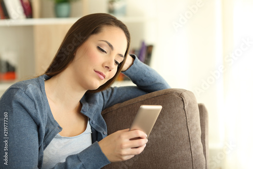 Serious girl reading messages in a smart phone at home